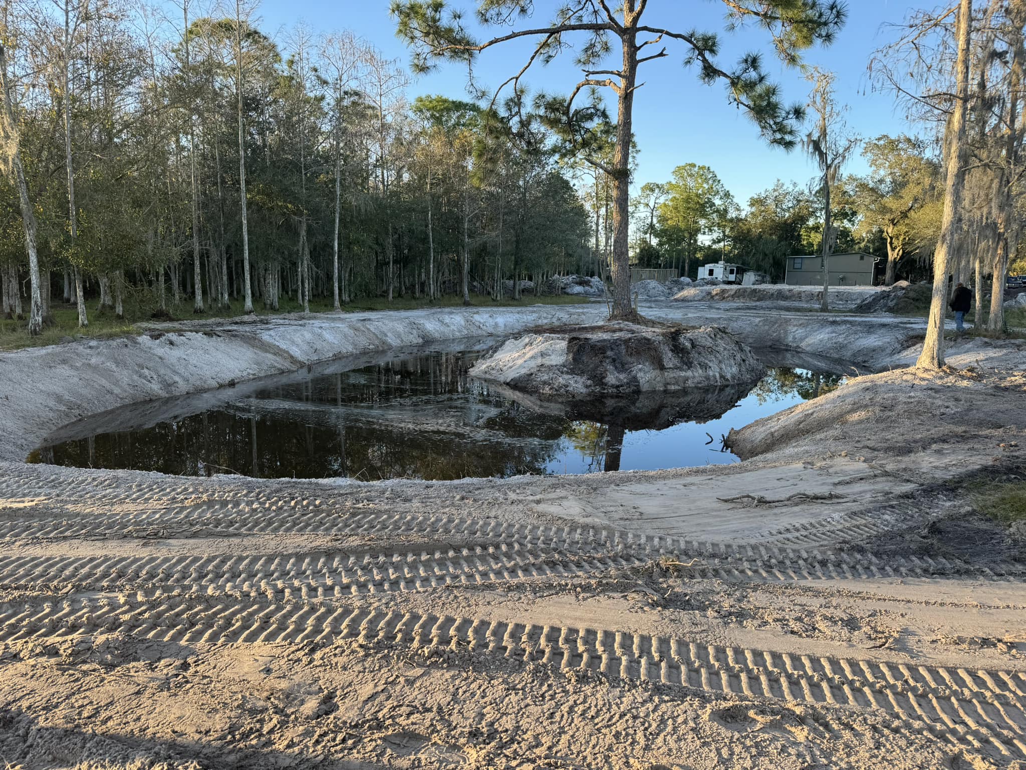 Excavated retention pond with tractor tracks in sandy Florida soil surrounded by pine trees